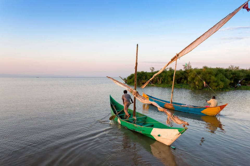 2 small boats with single sails furled each being paddled by a man on calm water