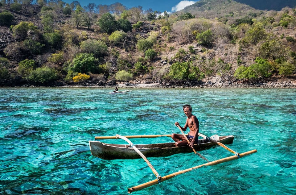 Man in an outrigger canoe on clear coastal waters in Indonesia